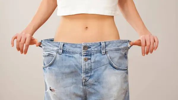 En person visar upp sina för stora jeans, ett tydligt tecken på att de lyckats gå ner i vikt.