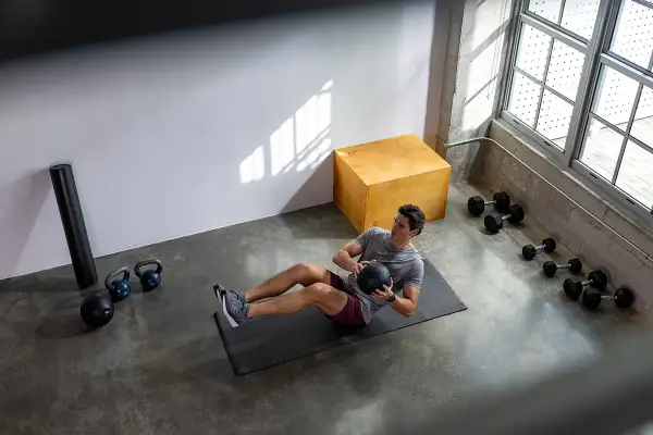 Man gör ett effektivt hiit pass hemma med en medicinboll. Träningsutrustning som kettlebells och hantlar syns i bakgrunden.
