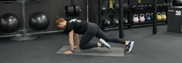 Kvinna gör mountain climbers på en träningsmatta i ett gym. Hon verkar ha dålig kondition, men kämpar på.